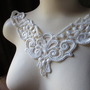 Op de afbeelding: Witte kantversiering met een delicaat bloemenpatroon. De versiering heeft een gegolfde rand en een hangende kwast.