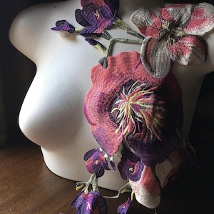 May include: Embroidered floral applique in shades of purple, pink, and green. The applique features large, detailed flowers and smaller buds, with a variety of textures and colors. The floral design is displayed on a white mannequin torso.