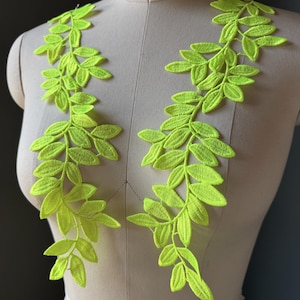 May include: A pair of neon yellow leaf-shaped embroidery appliques featuring intricate stitching details. These two symmetrical vine-like patches are designed to be attached to garments, showcasing a bright, vibrant color and detailed foliage patterns.