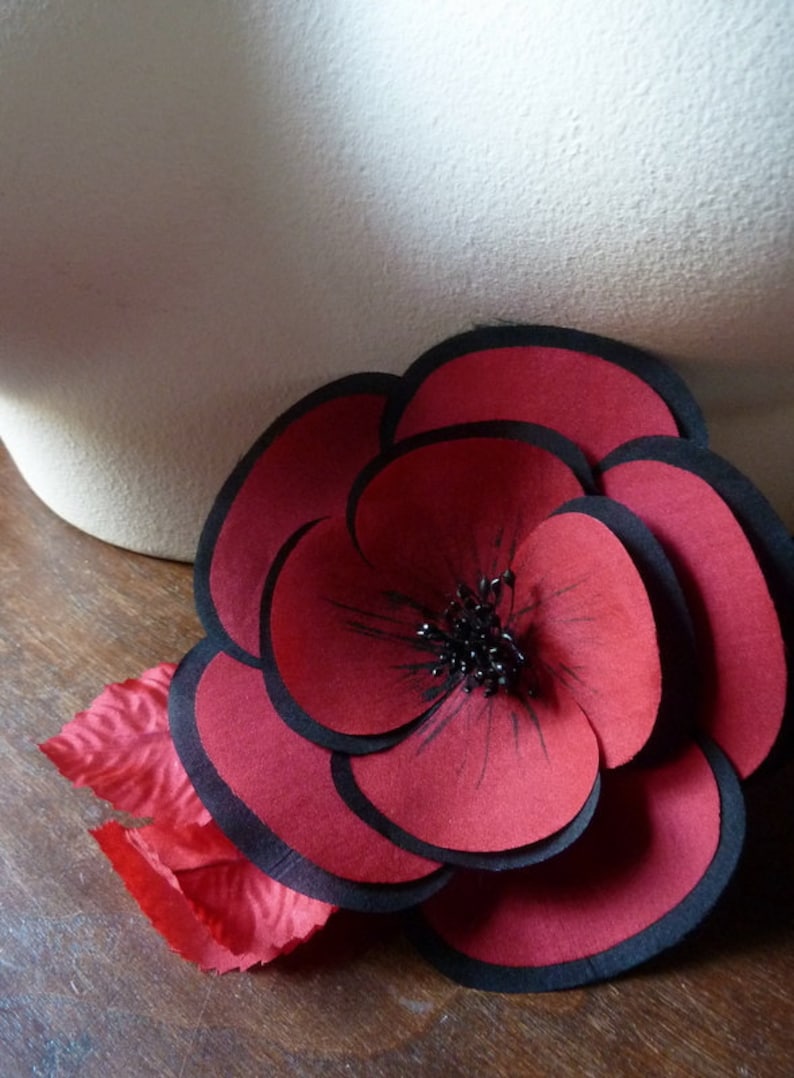 May include: A large red paper flower with black edges and a black center. The flower is made of multiple layers of paper.