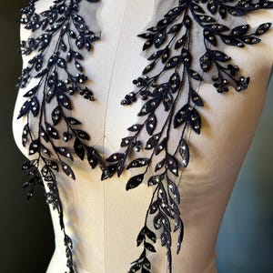 Könnte beinhalten: Schwarze Spitzenapplikation mit einem Blatt- und Rankenmuster, verziert mit glitzernden Strasssteinen. Die Applikation wird auf einer Schneiderpuppe präsentiert, um ihre filigranen Details hervorzuheben, ideal für Kleidung.