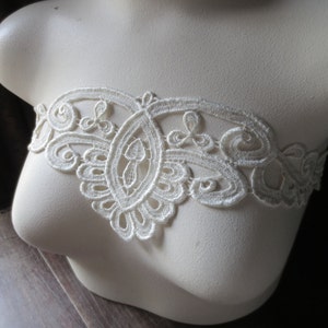 May include: White lace trim with a delicate floral pattern. The trim is shown on a white mannequin bust.