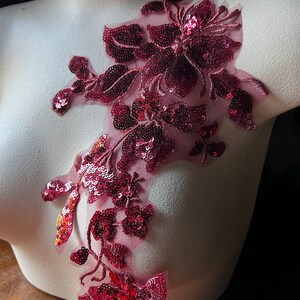 May include: A pink floral applique with sequins and a sheer mesh backing. The applique is perfect for adding a touch of elegance to any garment.