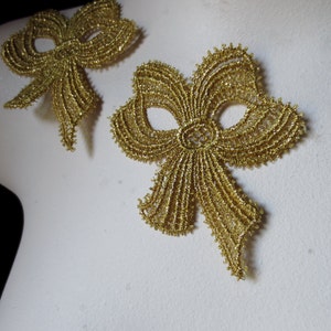 Może przedstawiać: Dwa złote koronkowe łuki z brokatem. Łuki są delikatne i misterne, z subtelnym wzorem siateczki.