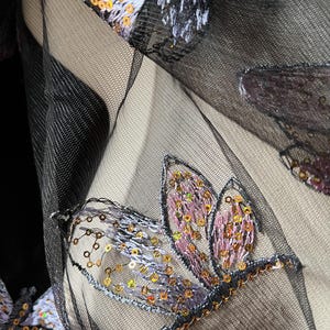 Puede incluir: Tela negra transparente con mariposas bordadas. Las mariposas están decoradas con lentejuelas iridiscentes.