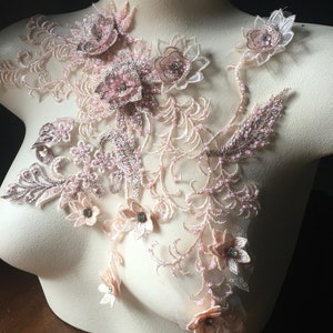 May include: A delicate floral lace applique with pink and beige flowers and beads. The applique features a variety of floral designs, including roses, lilies, and daisies. The applique is perfect for adding a touch of elegance to any garment or project.