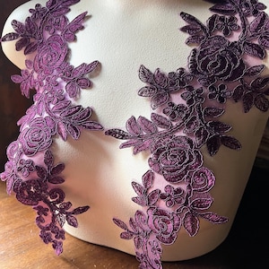 May include: Two pieces of purple floral lace applique with a delicate design. The lace features intricate floral patterns with a raised texture.
