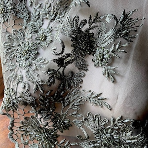 May include: Green beaded lace trim featuring floral and leaf designs. The lace is delicate and intricate, with small beads scattered throughout.