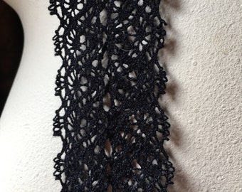 Puede incluir: Primer plano de un ribete de ganchillo negro con un diseño floral abierto. Los bordes del ribete tienen un patrón festoneado detallado, mientras que el centro tiene una estructura similar a una red. El color oscuro y los detalles intrincados sugieren un artículo artesanal.
