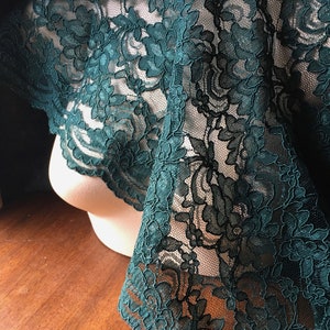 May include: Teal green lace fabric with a floral pattern. The lace is delicate and has a soft, flowing texture.