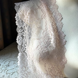 May include: A delicate, pale pink lace trim with a floral pattern. The lace is soft and flowing, with a delicate texture.