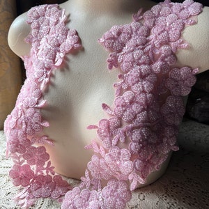 May include: Two pieces of pink beaded floral lace trim. The lace is made of delicate flowers and leaves.