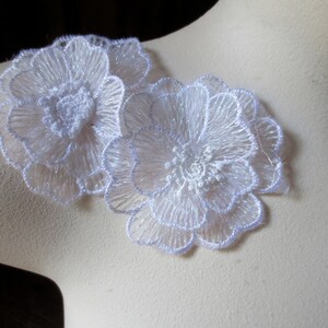 Puede incluir: Dos apliques de flores de encaje blanco con un diseño delicado y en capas. Los apliques están hechos de una tela transparente y ligera y tienen un brillo sutil.