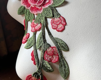 Puede incluir: Una aplicación floral bordada en rojo y verde con una rosa grande y flores más pequeñas en cascada por un tallo.