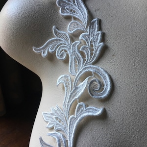 May include: White lace trim with a floral design. The lace is delicate and intricate, with a flowing pattern of leaves and swirls.