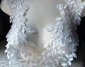 May include: Two white lace appliques with floral and leaf designs. The appliques are on a white mannequin bust.