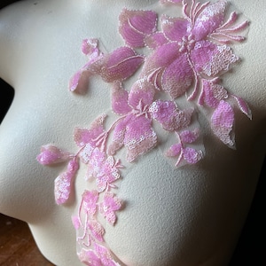 May include: Pink floral applique with sequins and beads. The applique is made of delicate fabric and features a variety of flower shapes.