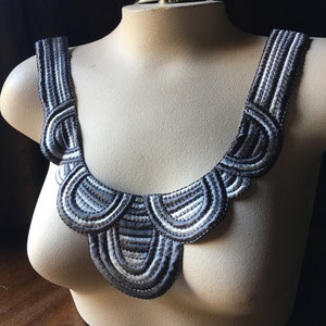 May include: A gray and white fabric trim with a scalloped design. The trim is made of multiple layers of fabric, creating a textured look.