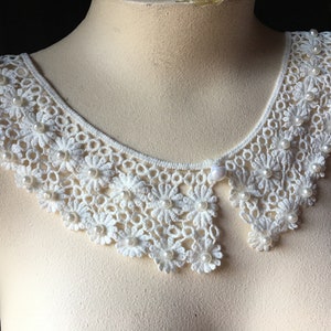 Puede incluir: Collar de encaje blanco con adornos de perlas. El collar es delicado y femenino, con un borde festoneado.