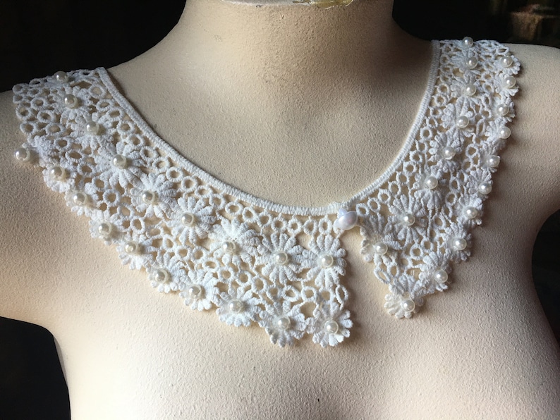 Puede incluir: Collar de encaje blanco con adornos de perlas. El collar es delicado y femenino, con un borde festoneado.
