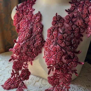 Puede incluir: Dos apliques florales burdeos con lentejuelas y cuentas. Los apliques están en un maniquí blanco y están listos para ser cosidos en una prenda.