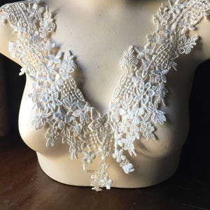 Op de afbeelding: Witte kantversiering met een bloemenpatroon, perfect om kleding of knutselwerk een vleugje elegantie te geven.