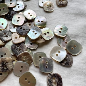 May include: A pile of iridescent, white, and brown shell buttons with two holes each. The buttons are square shaped with rounded corners.