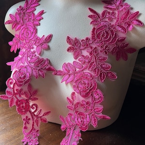 May include: Two pink floral lace appliques with a delicate floral design. The appliques feature a variety of flowers, including roses, and leaves. The lace is made of a soft, sheer fabric.