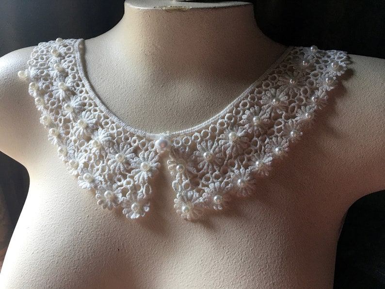 Puede incluir: Un cuello de encaje blanco con adornos de perlas. El cuello es delicado y femenino, y ser&iacute;a perfecto para agregar un toque de elegancia a cualquier atuendo.