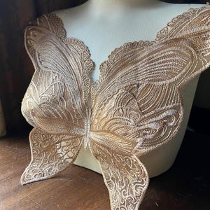 Può includere: Un'applicazione in pizzo dorata a forma di farfalla. Il pizzo è intricato e dettagliato, con un delicato motivo floreale. Questa applicazione sarebbe perfetta per aggiungere un tocco di eleganza a un capo di abbigliamento o un progetto artigianale.