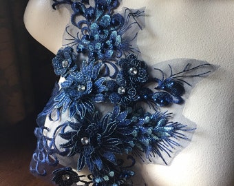 May include: A navy blue lace applique with floral and beaded embellishments. The applique features intricate embroidered details, sparkling rhinestones, and small, dark blue beads. The design is displayed on a mannequin, showcasing the delicate craftsmanship and texture.