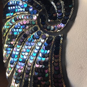May include: A black fabric applique with iridescent blue and green sequins arranged in a swirling pattern. The sequins are sewn onto a black fabric base.