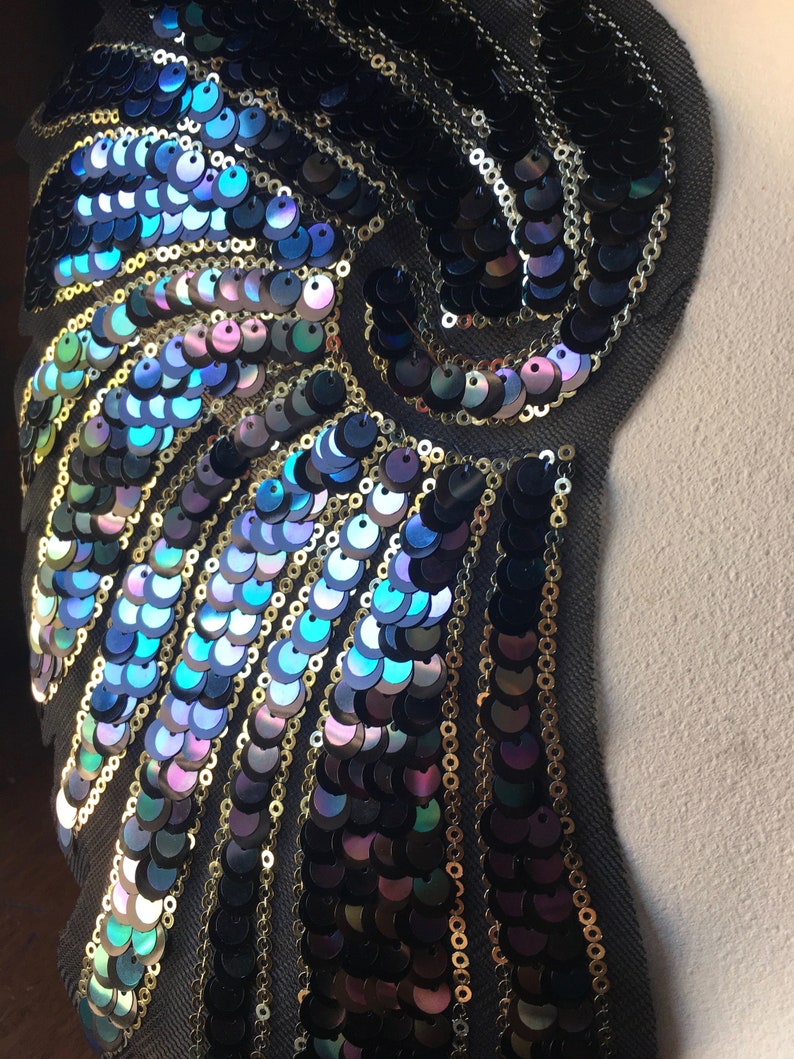 May include: A black fabric applique with iridescent blue and green sequins arranged in a swirling pattern. The sequins are sewn onto a black fabric base.