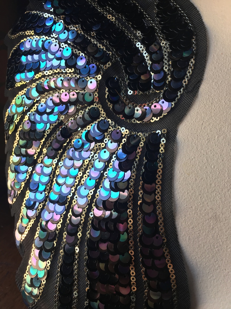 May include: A black fabric applique with iridescent blue and purple sequins arranged in a swirling pattern.