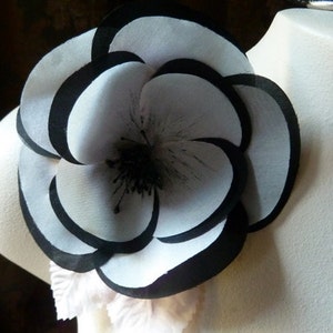 May include: A large, white fabric flower with black trim. The flower has multiple layers and a black center.