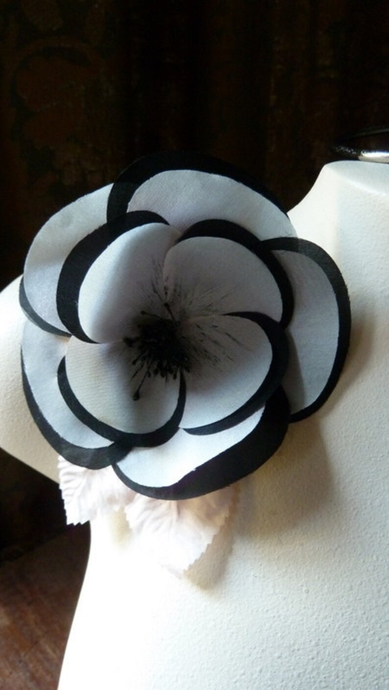 May include: A large, white fabric flower with black trim. The flower has multiple layers and a black center.