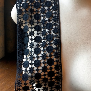 May include: A length of navy blue lace with a repeating pattern of circles and floral elements. The lace is draped over a white mannequin, showcasing its openwork design and intricate details. The lace is likely used for sewing or crafting.