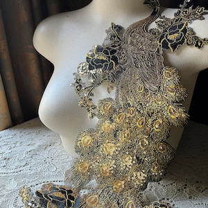 Peut inclure: Un motif de paon brodé en or et noir avec des paillettes. Le paon est debout sur une surface blanche.