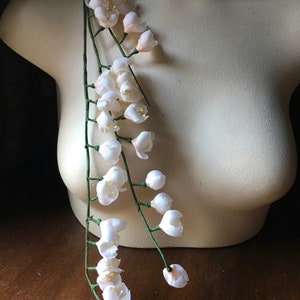 May include: A long strand of white artificial flowers with green stems. The flowers are arranged in clusters along the stems.