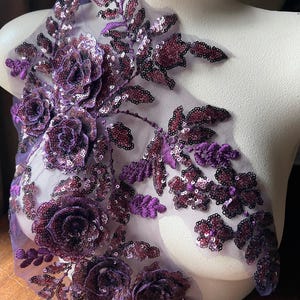 May include: Purple floral applique with sequins and beads on a mesh fabric. The applique features a cluster of roses and leaves.