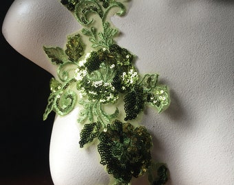 May include: Green floral applique with sequins. The applique features a large flower with smaller flowers and leaves. The applique is made of a sheer fabric with sequins sewn on.