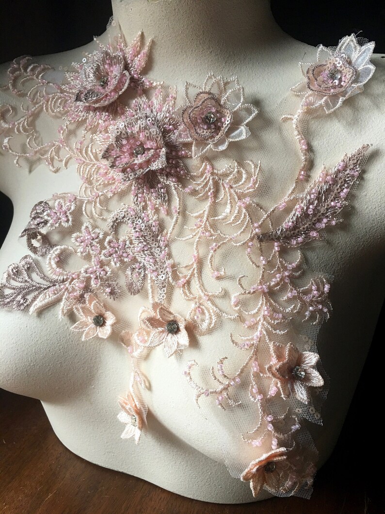 May include: A delicate floral applique with pink and beige embroidery and beads. The applique features a variety of flowers and leaves, and is perfect for adding a touch of elegance to any project.