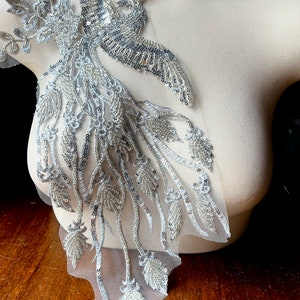 May include: A silver and white beaded phoenix applique with a long tail of beaded leaves. The applique is on a sheer mesh fabric.
