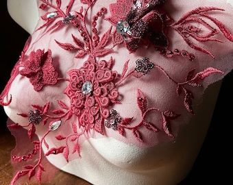 May include: Burgundy red lace applique with floral designs, sequins, and rhinestones. The applique is on a white mannequin bust.