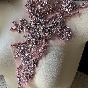 Puede incluir: Una aplicaci&oacute;n de cuentas y diamantes de imitaci&oacute;n de color rosa con un dise&ntilde;o floral. La aplicaci&oacute;n est&aacute; sobre un fondo de tela transparente.