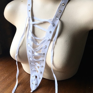 May include: White cotton fabric with grommets and laces tied in a criss-cross pattern. The fabric is draped over a white mannequin.