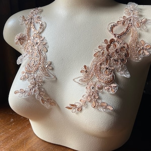 Puede incluir: Dos delicados apliques de encaje con un diseño floral en color oro rosa. Los apliques están hechos de una tela transparente con lentejuelas y cuentas.