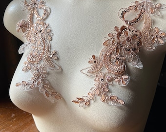 May include: Two delicate lace appliques with a floral design in a rose gold color. The appliques are made of a sheer fabric with sequins and beads.