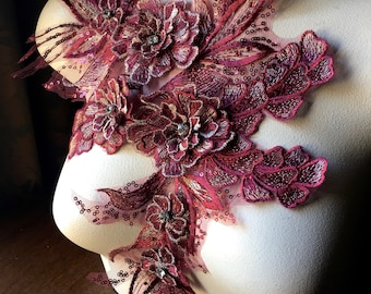 Op de afbeelding: Bordeauxrode bloemenapplicatie van kant met pailletten en strass. De applicatie heeft een cluster van driedimensionale bloemen met delicate bladeren en ingewikkelde details.