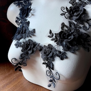 Peut inclure: Deux appliques en dentelle noire avec des motifs floraux en forme de roses 3D. Les appliques sont sur un buste de mannequin blanc.